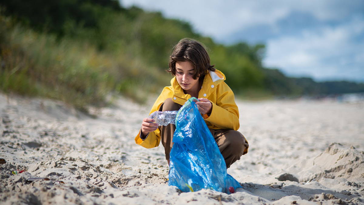 A boy collects old discarded plastic bottles on the coast to recycle them