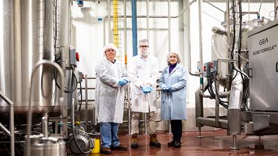 Michael Harrison, Christopher Conner, and Robin Conner (left to right) holding spray dried product standing near GEA’s INLINE FORMULA® high shear mixer (right of photo)